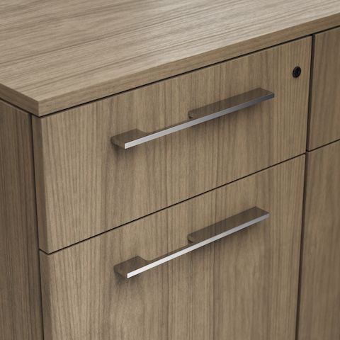 Detail shot of the Geiger One Casegoods asymmetrical pull option in Chrome on a Natural Flat Cut Walnut drawer front viewed from an angle.