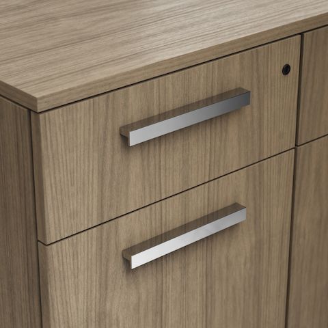Detail shot of the Geiger One Casegoods ledge pull option in Chrome on a Natural Flat Cut Walnut drawer front viewed from an angle.