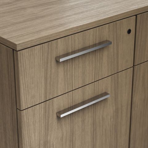 Detail shot of the Geiger One Casegoods façade pull option in Chrome on a Natural Flat Cut Walnut drawer front viewed from an angle.
