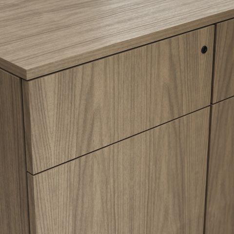 Detail shot of the Geiger One Casegoods no pull, push to open option on a Natural Flat Cut Walnut drawer front viewed from an angle.