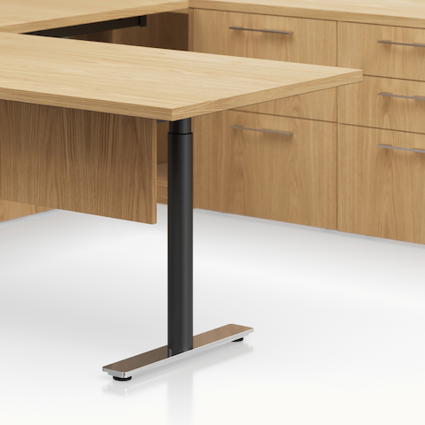 Detail shot of the Geiger One Casegoods t-foot leg option with a black column and chrome foot in a Natural Flat Cut Oak private office.