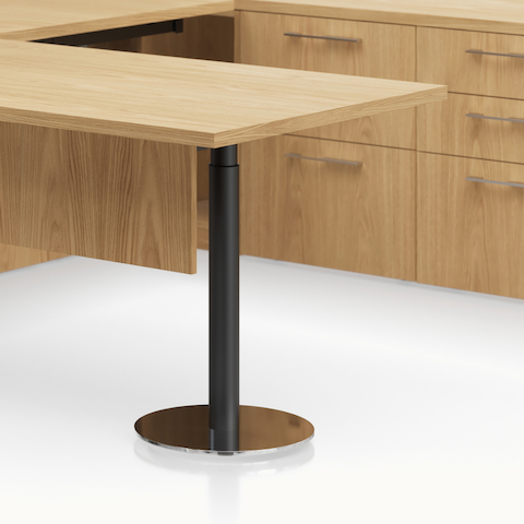 Detail shot of the Geiger One Casegoods disc foot leg option with a black column and chrome foot in a Natural Flat Cut Oak private office.